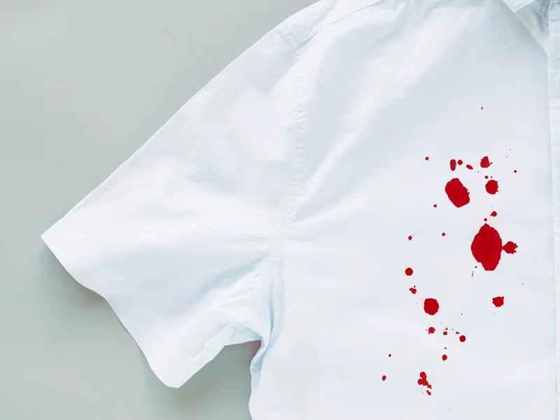 White button-up shirt with red stains or blood splatters on the fabric against a light background.