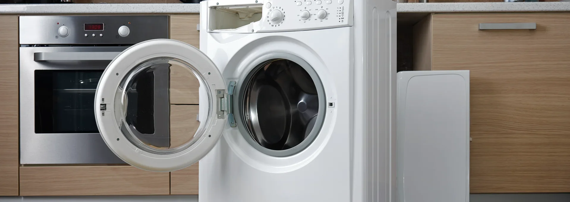 White washing machine with open door in modern kitchen, with toolbox and repair tools on floor.
