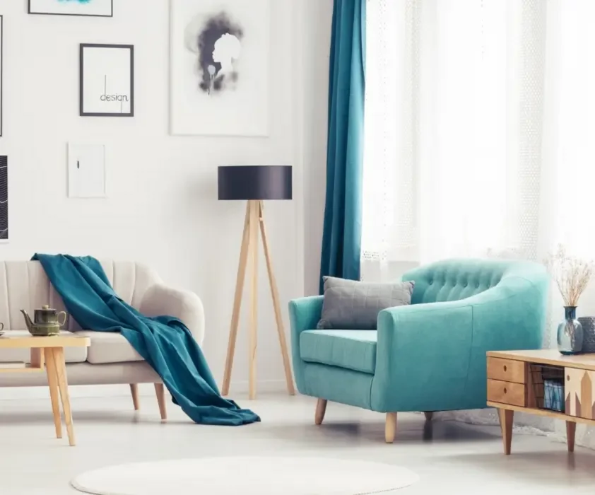 Phòng khách hiện đại với ghế xanh ngọc, sofa kem, đèn sàn gỗ, rèm xanh và tranh treo tường tối giản.