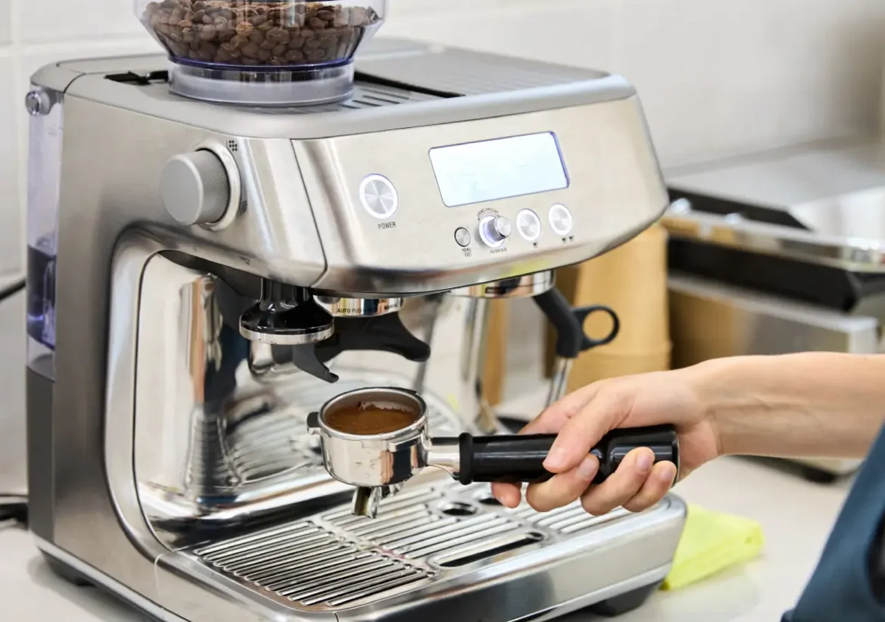 Người dùng đang sử dụng máy pha cà phê tự động bằng thép không gỉ, rút portafilter chứa cà phê đã pha xong.