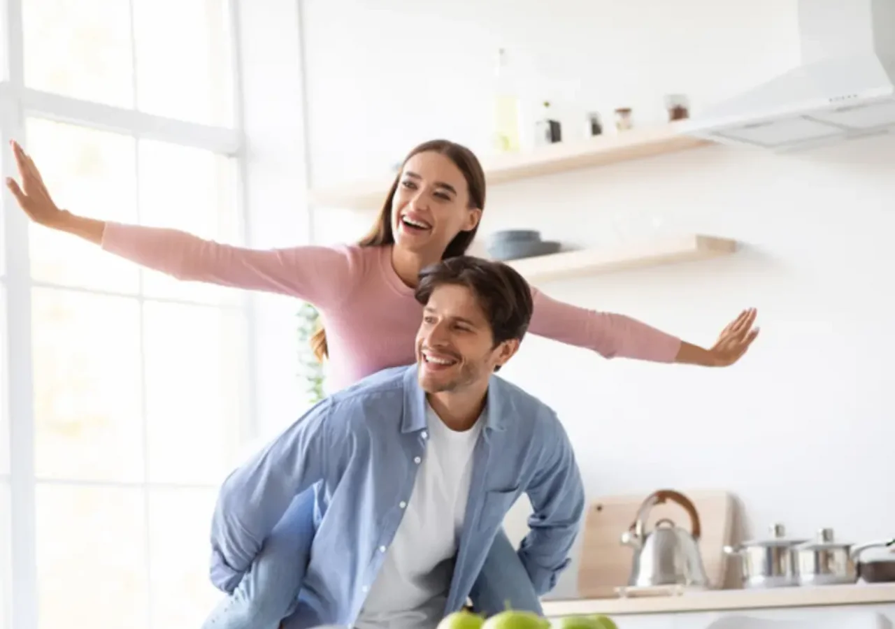 Cặp đôi trẻ vui vẻ trong bếp hiện đại, người phụ nữ xoay tay ra sau lưng người đàn ông, quầu xanh trên bàn bếp.