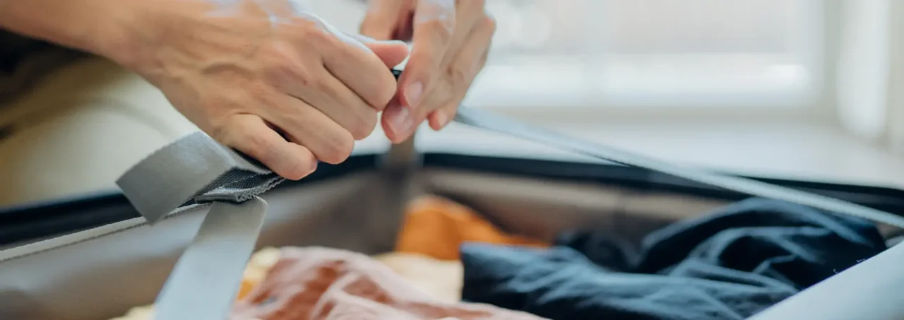 Tay người đóng gói quần áo vào hộp, có các loại quần áo màu cam và xanh được sắp xếp bên trong.