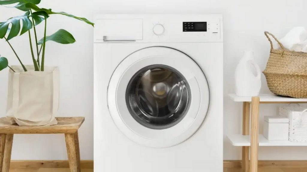 Máy giặt trắng hiện đại đặt trong phòng laundry sạch sẽ, xung quanh là cây xanh và giỏ đựng quần áo.