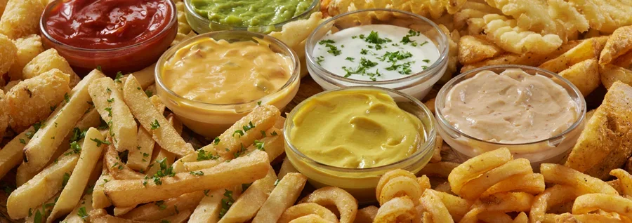 Assorted fried foods with dipping sauces including fries, onion rings, and waffle fries arranged on a wooden board.