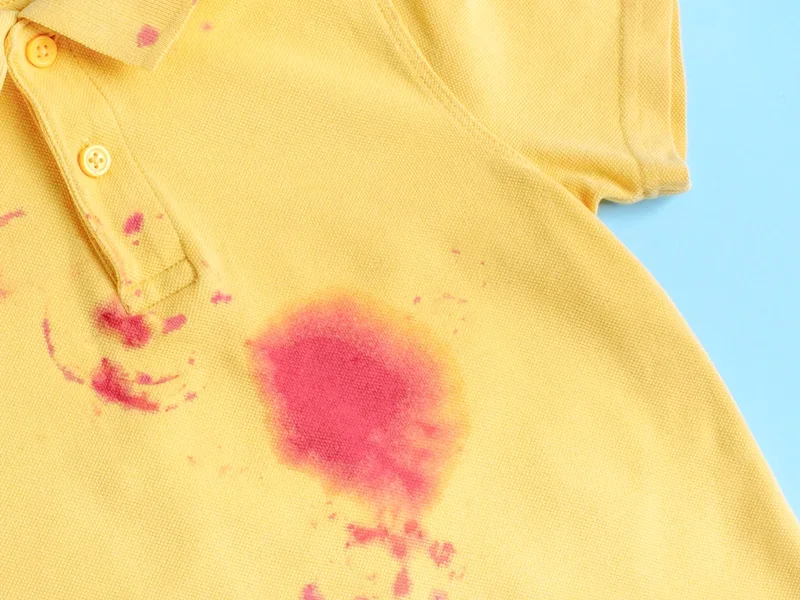 Yellow polo shirt with pink stains and splashes against a blue background.