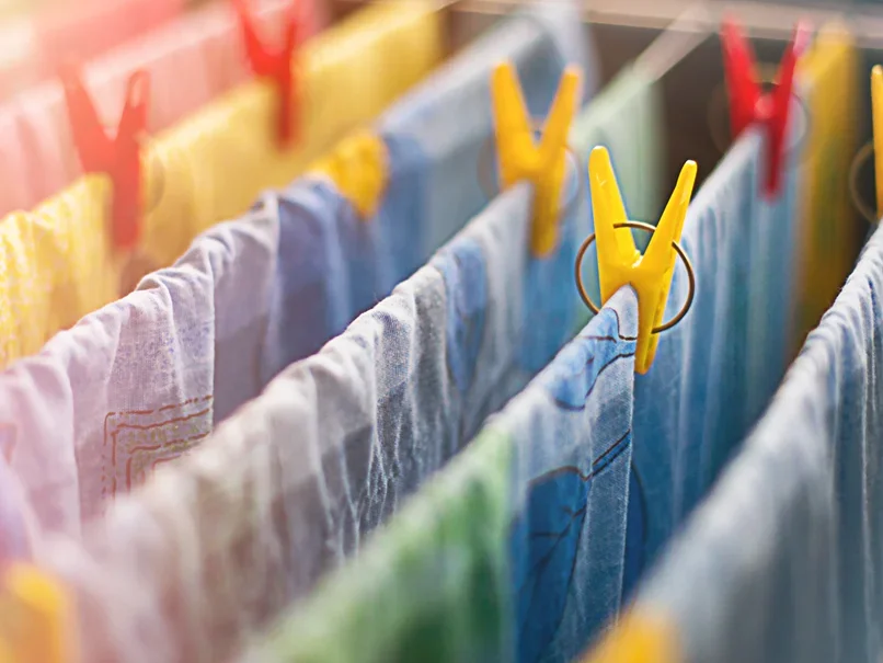 Colorful clothes hanging on a clothesline with yellow clothespins in bright sunlight.