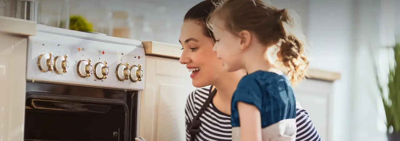 Một người phụ nữ và một bé gái đang mở cửa lò nướng trong bếp hiện đại, cười vui vẻ.