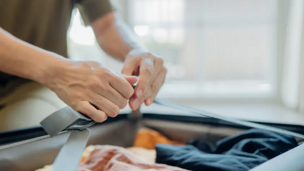 Tay người phụ nữ gấp quần áo màu sắc khác nhau trong hộp gần cửa sổ.