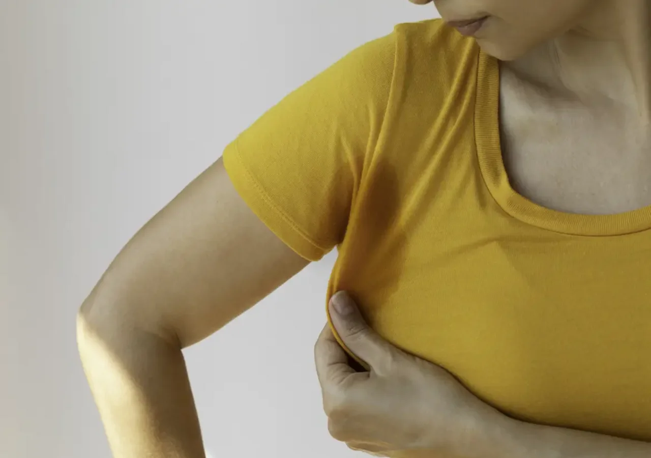 Người phụ nữ mặc áo màu vàng kéo chiếc áo thun lên dưới nách; ở đó có một vết ướt
